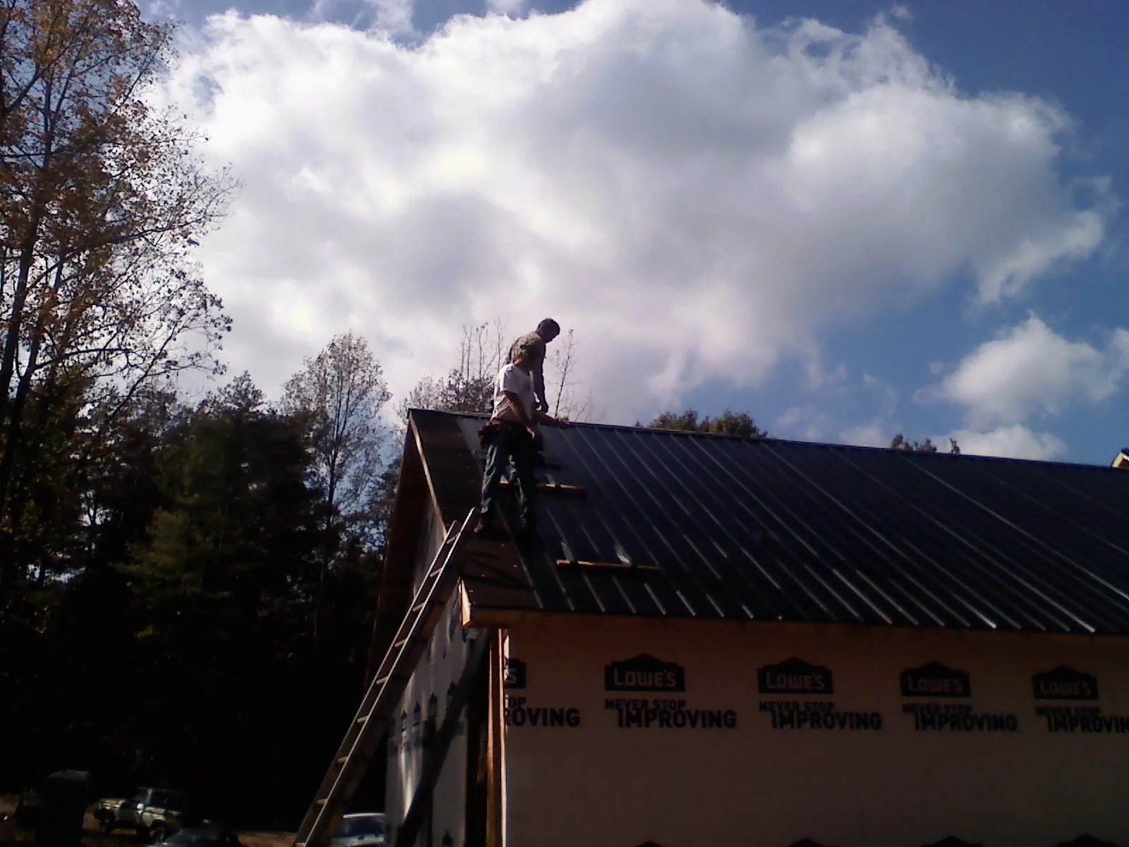Roofer fastening dark metal panels high against a cloudy sky, from a Roof Inspection job in Coolidge